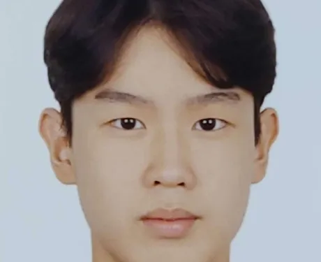 Photo of a young Korean boy from the shoulders up. He is wearing a black top and has dark brown hair and brown eyes.