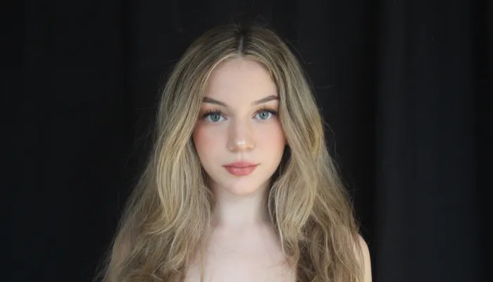 Photo of a teenage girl with white skin and long brownish-blondish standing against a black background.