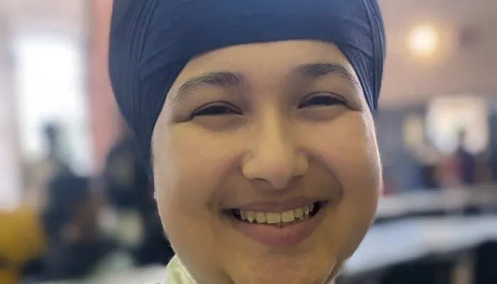 Photo of a smiling sikh girl wearing a white and blue plaid shirt and a dark blue turban.
