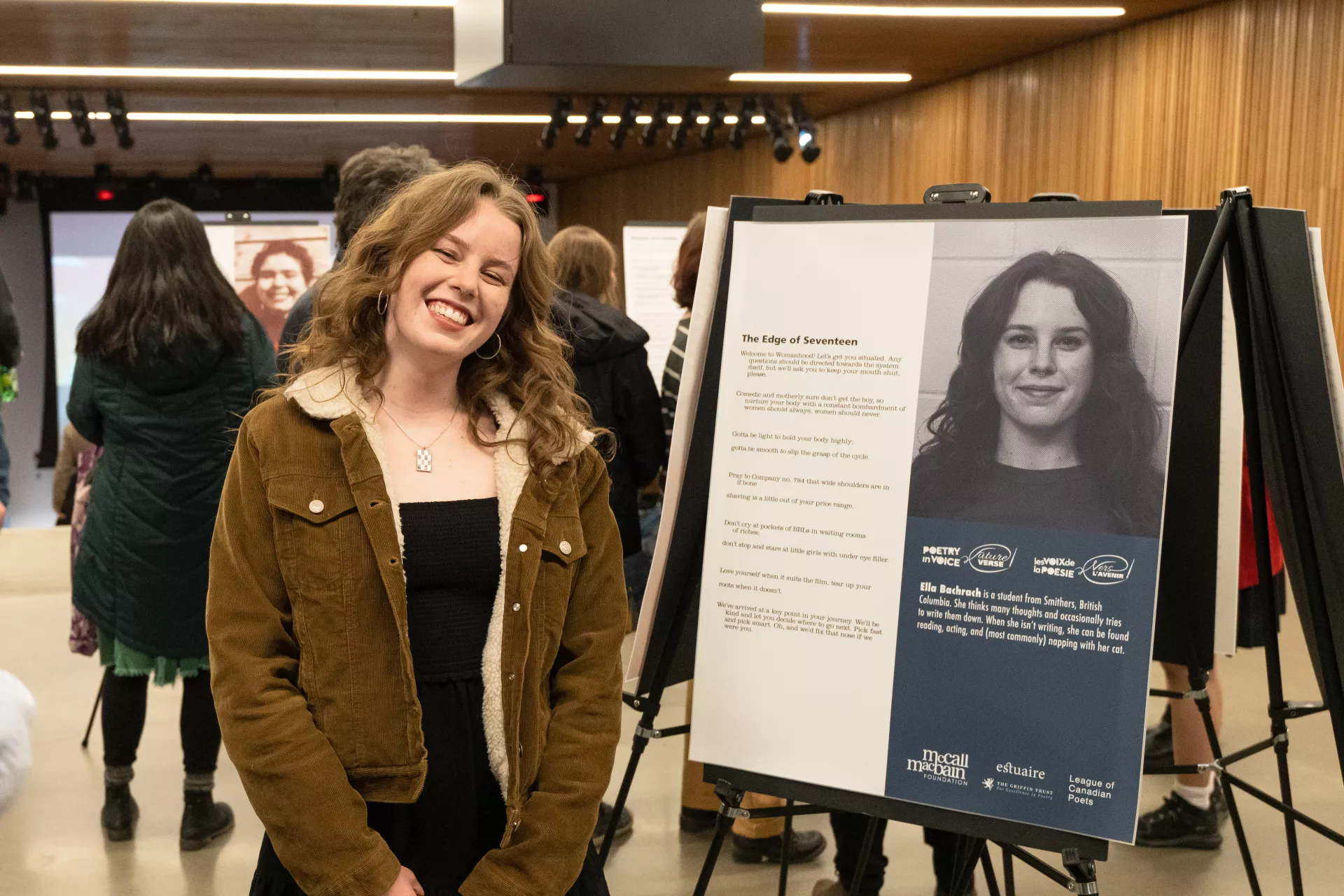 Ella Bachrach proudly standing beside the poster featuring the poem that allowed her a spot in the FutureVerse program.
